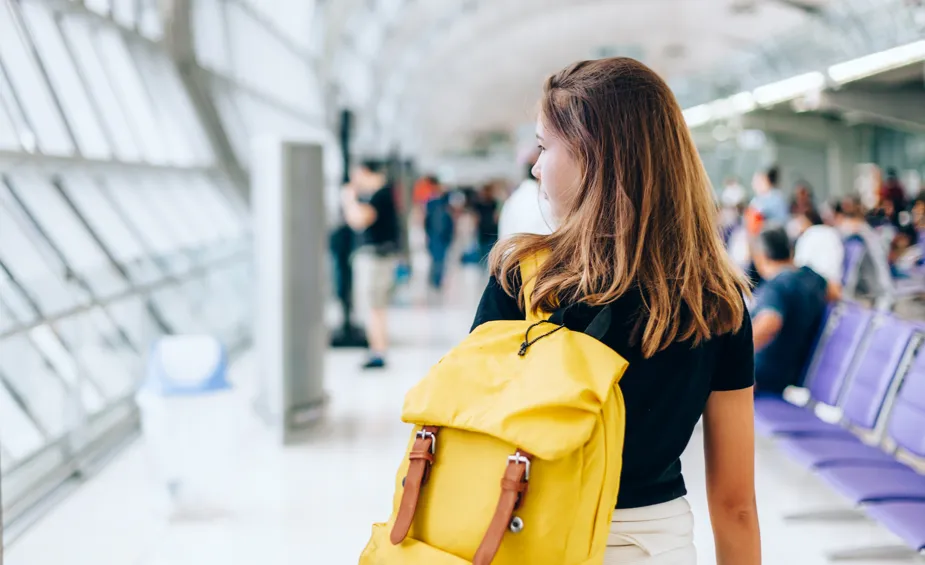 A woman with a yellow backpack walking through an airport.