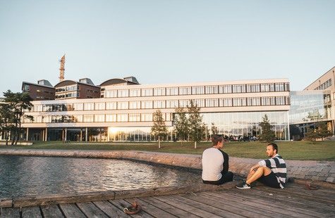 Foto på två studenter som sitter på badbryggan utanför Campus Gräsvik