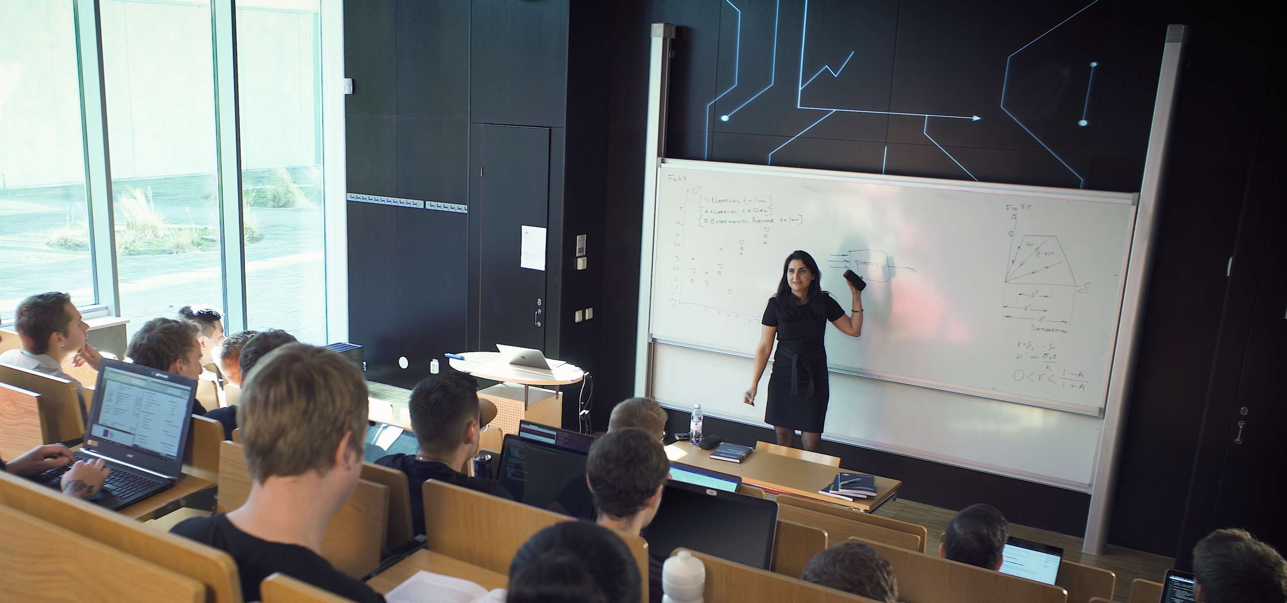 Lärare. står vid whiteboard och föreläser för studenter