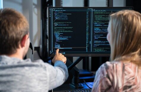 Två studenter vid en skärm med datorkod. Den ena studenten pekar på skärmen.