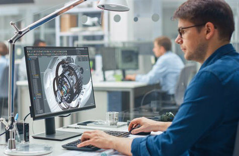 Kille som sitter och 3D-modellerar vid en dator på ett kontor.